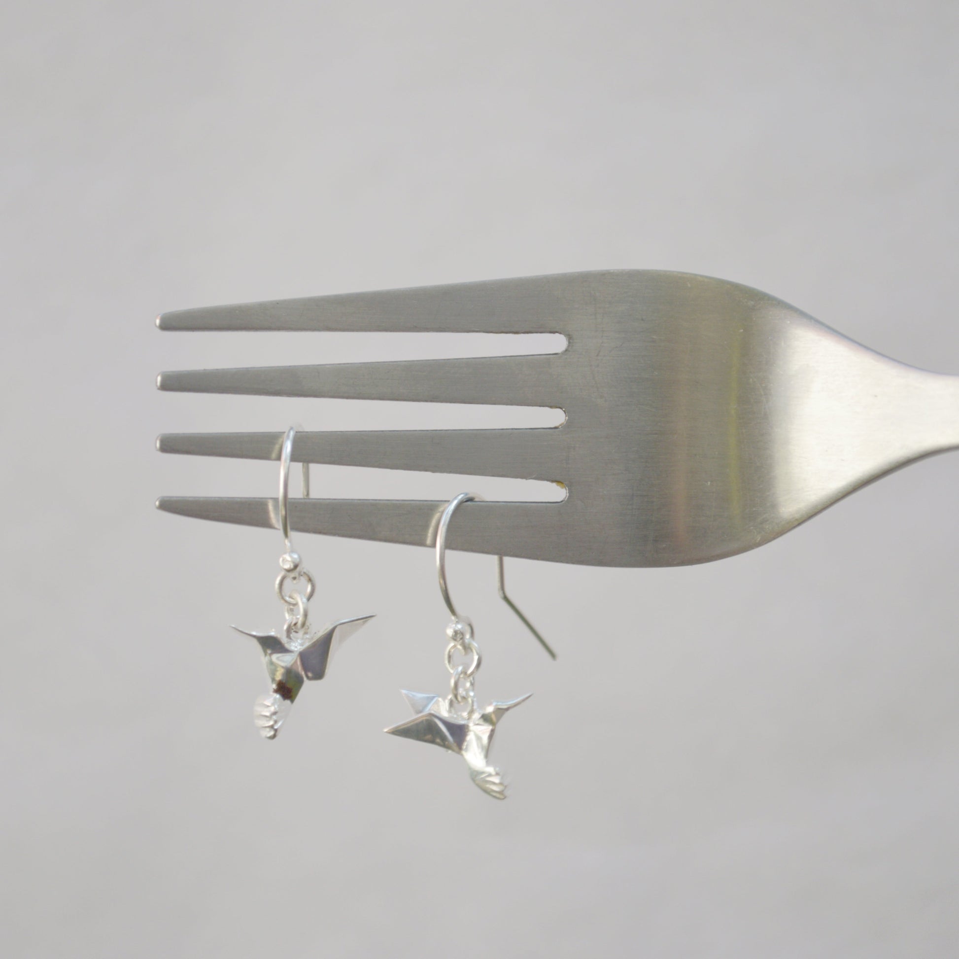 aretes colibrí de plata puestos en un tenedor.